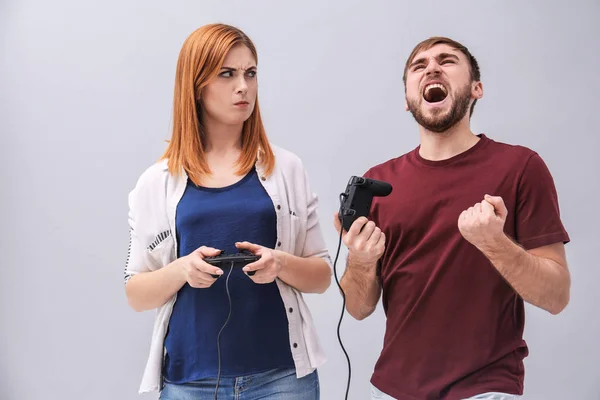 Emocionální pár s video herní zařízení na šedém pozadí — Stock fotografie