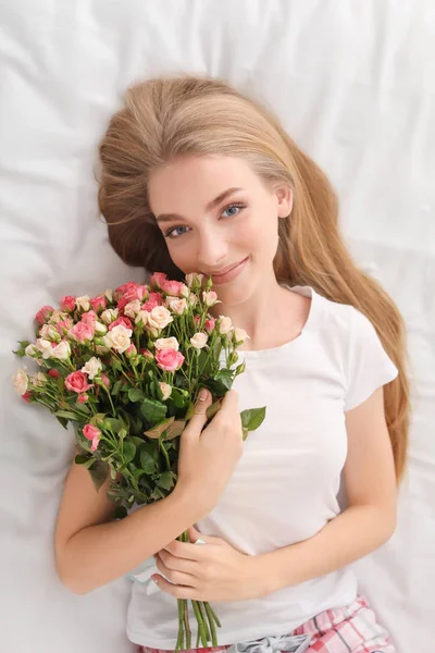 Hermosa joven con ramo de rosas en la cama en casa — Foto de Stock