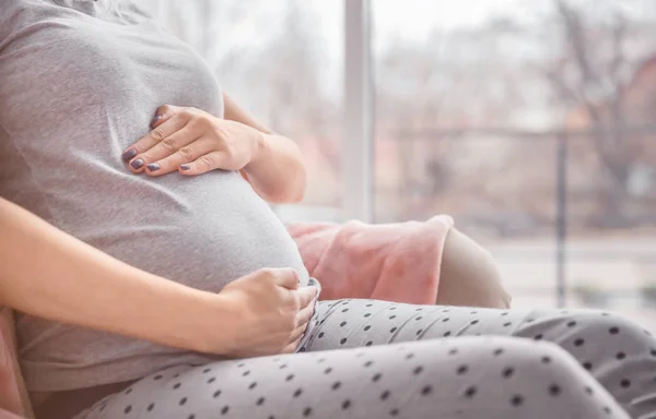 Mulher grávida de mãos dadas na barriga dentro de casa — Fotografia de Stock