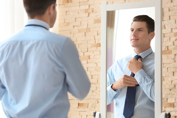 Young businessman looking at himself in mirror indoors