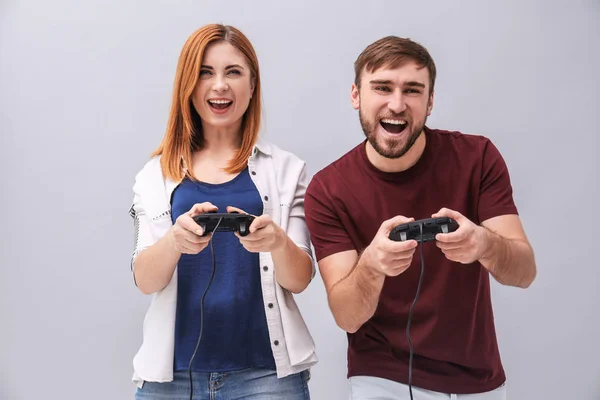 Emotionales Paar mit Videospiel-Controllern auf grauem Hintergrund — Stockfoto