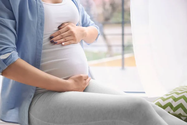 Pregnant woman holding hands on belly indoors — Stock Photo, Image