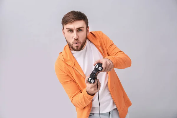 Homem emocional com controlador de videogame em fundo cinza — Fotografia de Stock