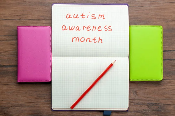 Notebook z frazą "Autism awareness month" na podłoże drewniane — Zdjęcie stockowe