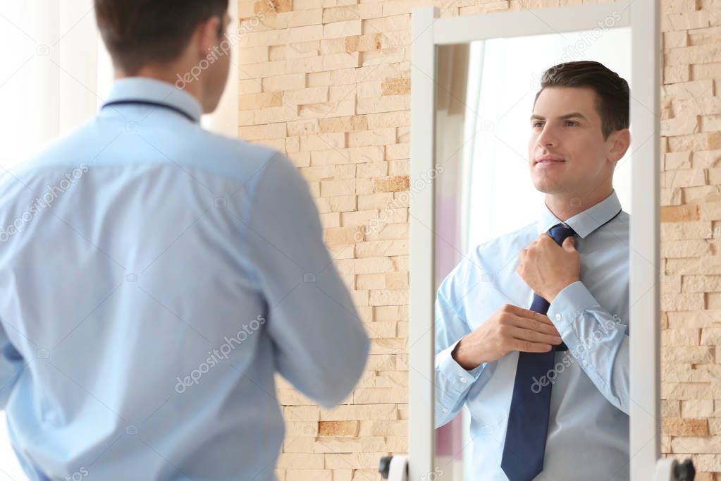 Young businessman looking at himself in mirror indoors