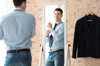Young businessman looking at himself in mirror indoors clipart