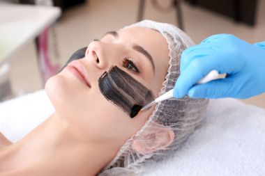 Cosmetologist applying carbon nanogel on woman's face, closeup. Peeling procedure clipart