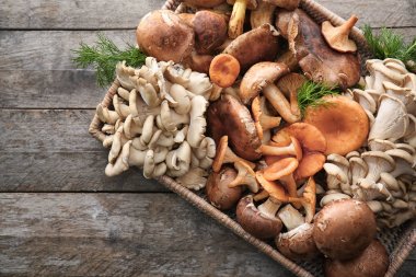 Wicker tray with variety of raw mushrooms on wooden table clipart