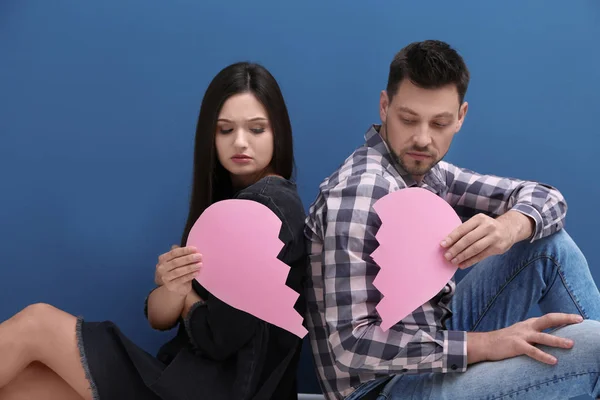 Молодая пара держит разрезанное пополам бумажное сердце на цветном фоне. Проблемы отношений — стоковое фото