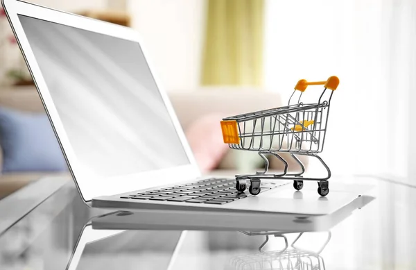 Laptop en klein winkelwagentje op tafel. Internet shopping concept — Stockfoto