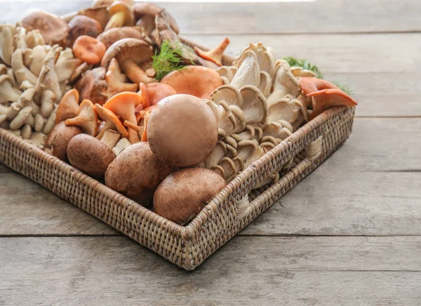 Vassoio di vimini con varietà di funghi crudi sul tavolo di legno — Foto Stock