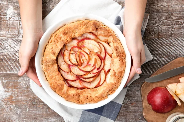 Женские руки со свежеприготовленным яблочным пирогом на деревянном фоне — стоковое фото