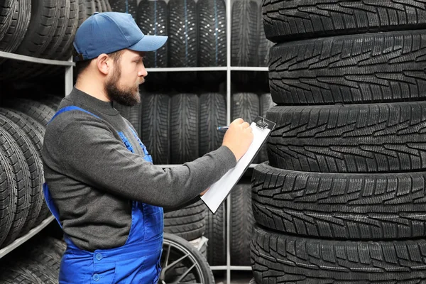 Meccanico maschio con appunti vicino pneumatici auto in negozio di automobili — Foto Stock