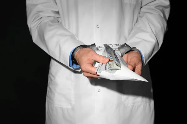 Doctor in de handboeien houden van smeergeld op zwarte achtergrond, close-up — Stockfoto