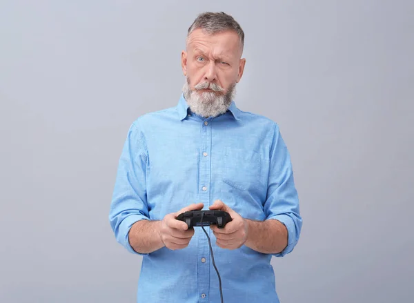 Emocional hombre mayor jugando videojuego sobre fondo gris — Foto de Stock