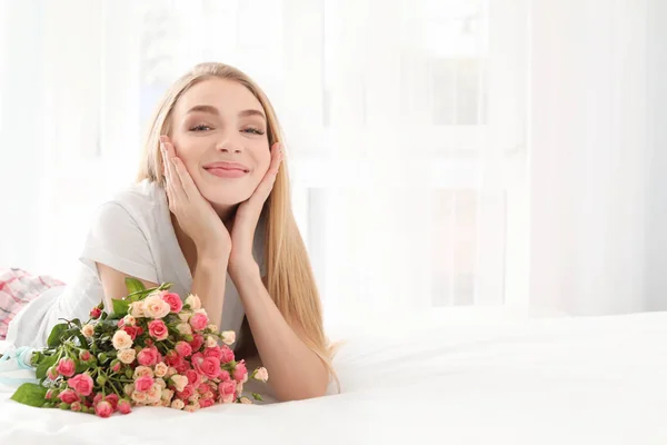 Beautiful young woman with bouquet of roses on bed at home — Stock Photo, Image