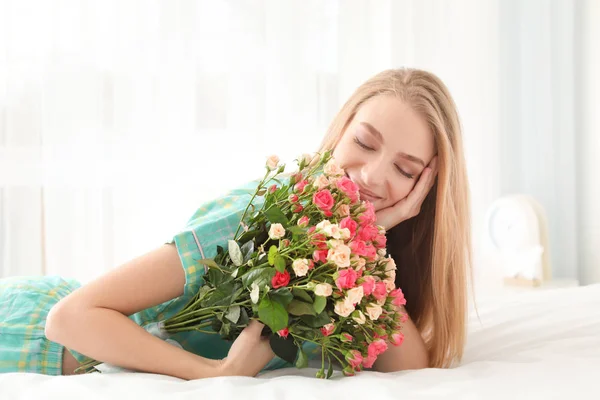 Mulher bonita com buquê de rosas na cama em casa — Fotografia de Stock