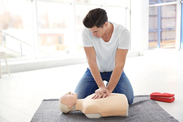Young man practicing first aid on mannequin indoors — Stock Photo, Image