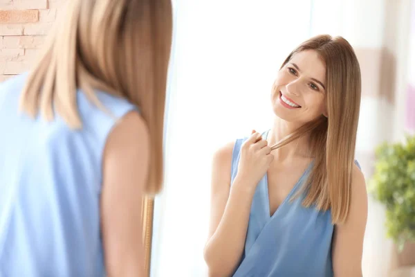 Young woman looking at herself in mirror indoors — Stock Photo, Image
