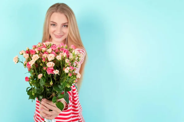 Krásná mladá žena s kyticí růží na barevném pozadí — Stock fotografie