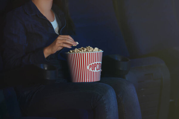Young woman with cup of tasty popcorn in cinema