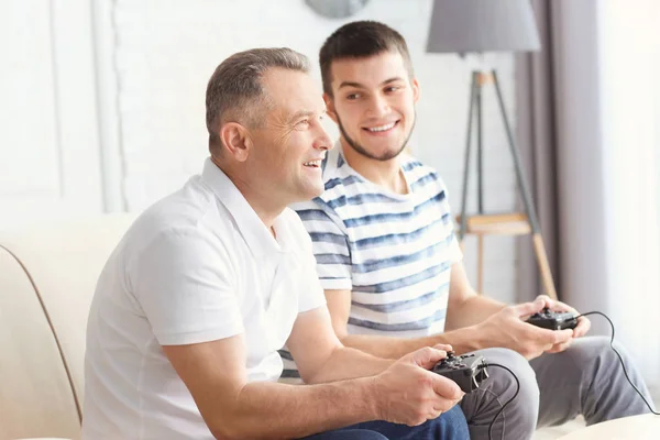 Зрелый мужчина играет в видеоигры со своим сыном дома — стоковое фото