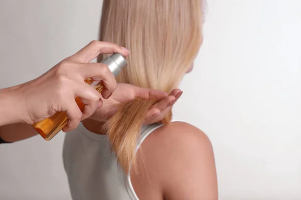 Stylist applying oil onto woman's hair on light background — Stock Photo, Image