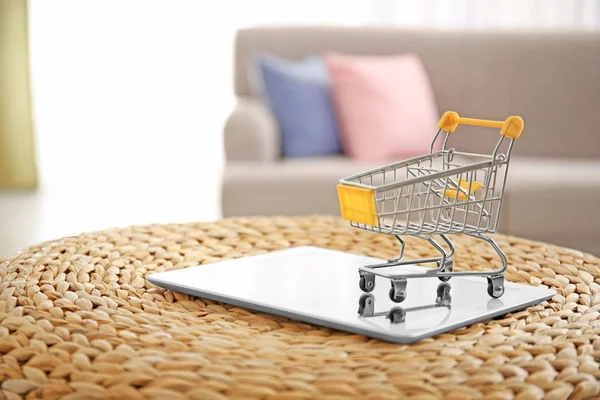 Tablet computer and small shopping cart on wicker pouf. Concepto de compras por Internet —  Fotos de Stock