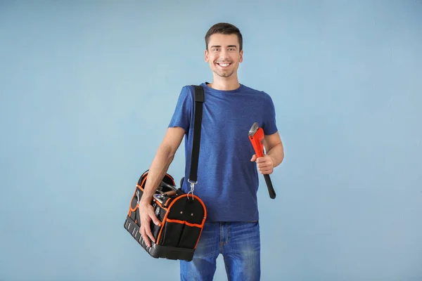 Joven fontanero con bolsa de herramientas y llave de tubo sobre fondo de color — Foto de Stock