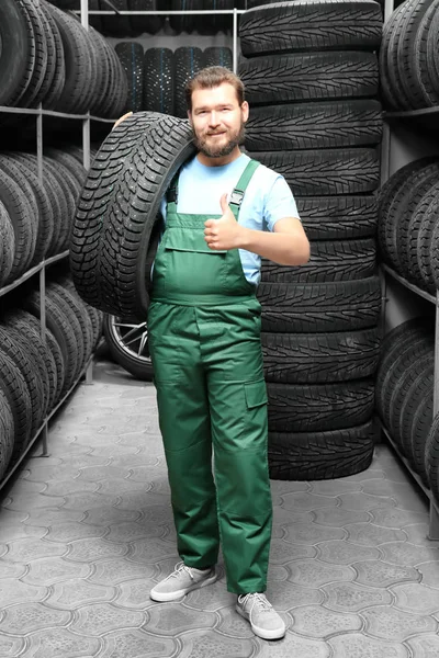 Male mechanic with car tire in automobile store