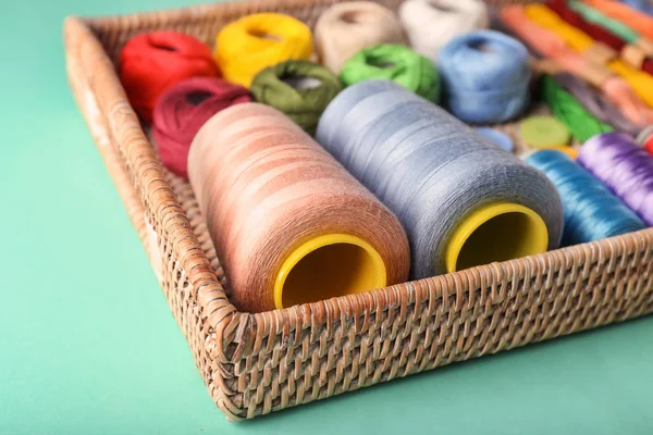 Bandeja de mimbre con hilos de coser sobre fondo de color, primer plano —  Fotos de Stock