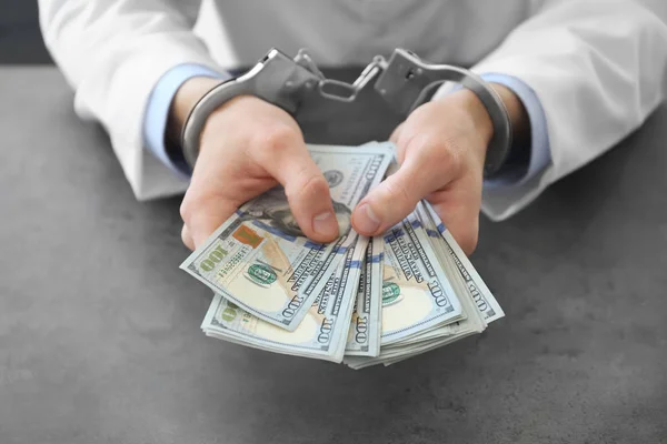 Doctor in handcuffs holding bribe at workplace, closeup — Stock Photo, Image