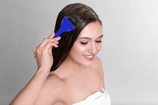 Young woman applying mask onto her hair on light background — Stock Photo, Image