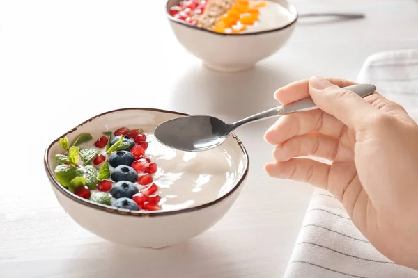 Mujer comiendo sabroso yogur con semillas de arándano y granada en la mesa de madera — Foto de Stock