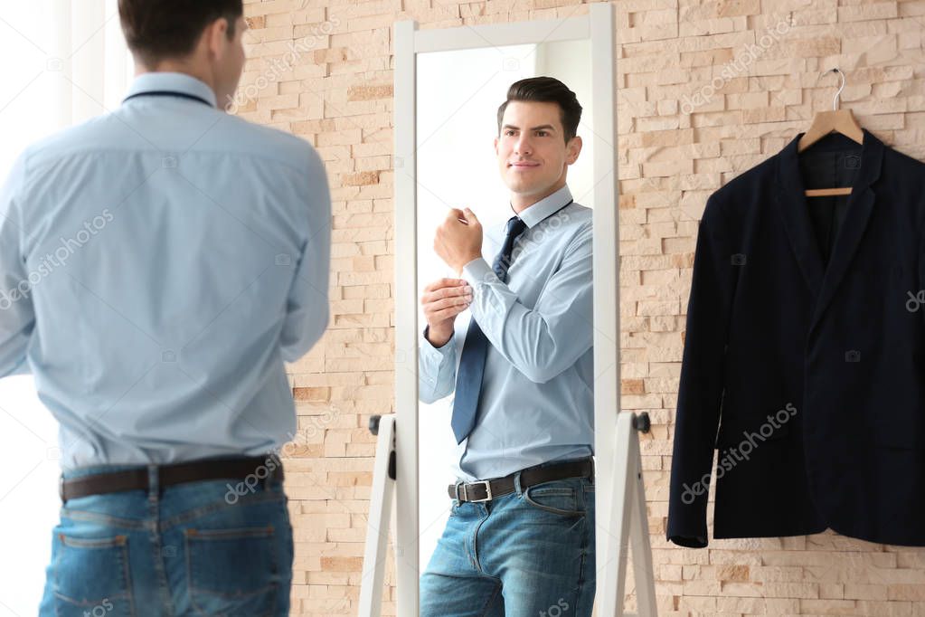 Young businessman looking at himself in mirror indoors
