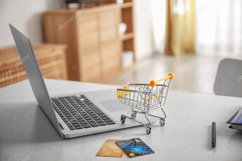 Laptop, small shopping trolley and credit cards on table. Internet shopping concept