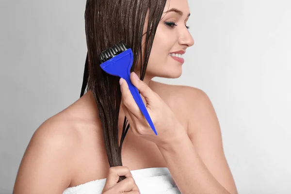 Young woman applying mask onto her hair on light background — Stock Photo, Image