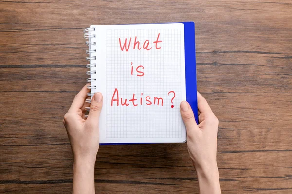 Mujer sosteniendo un cuaderno con la frase "¿Qué es el autismo?" sobre fondo de madera — Foto de Stock