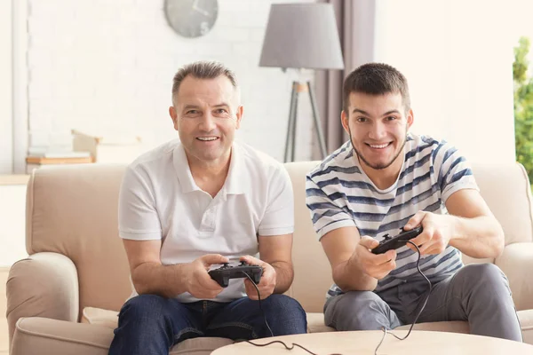 Зрелый мужчина играет в видеоигры со своим сыном дома — стоковое фото