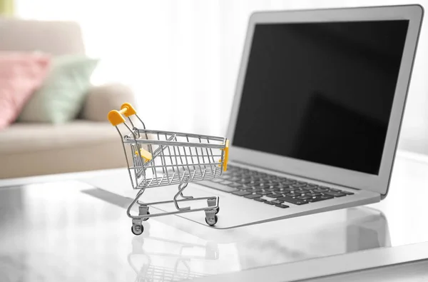 Laptop en klein winkelwagentje op tafel. Internet shopping concept — Stockfoto