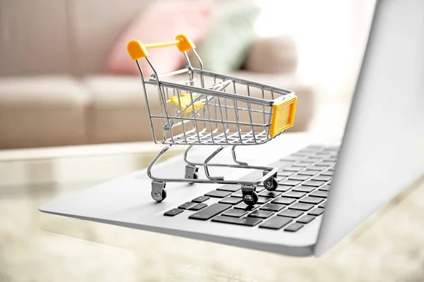 Laptop a malý nákupní košík na stole. koncept internetového nakupování — Stock fotografie