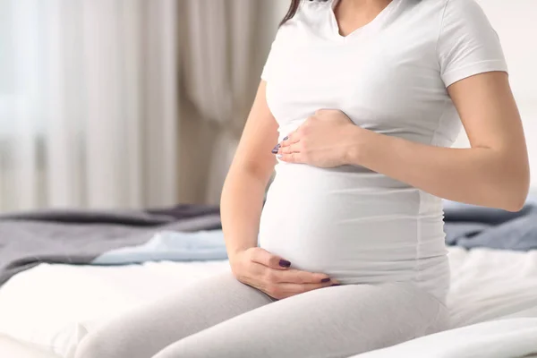 Mujer embarazada cogida de la mano en el vientre en el interior — Foto de Stock