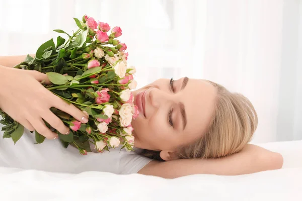 Mooie jonge vrouw met boeket rozen op bed thuis — Stockfoto