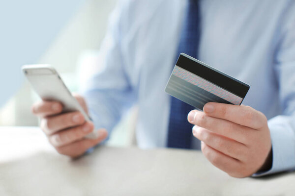 Человек с кредиткой и мобильным телефоном, в помещении
