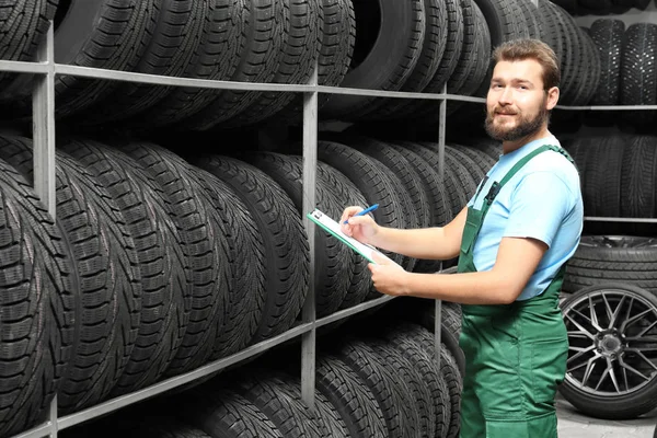 Mecánico masculino con portapapeles cerca de neumáticos de automóviles en la tienda de automóviles —  Fotos de Stock