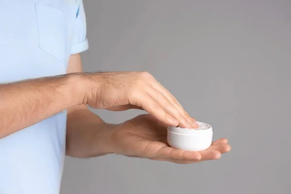 Hombre aplicando crema de manos sobre fondo gris — Foto de Stock