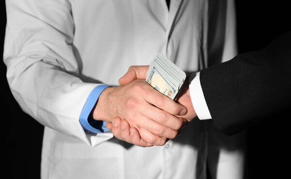 Врач получает взятку от бизнесмена на черном фоне, крупным планом
