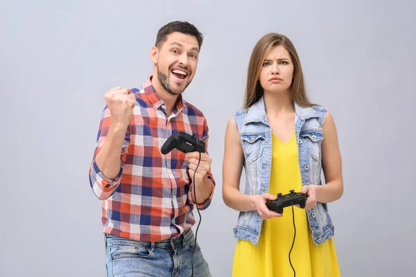 Casal emocional com controladores de videogame em fundo cinza — Fotografia de Stock