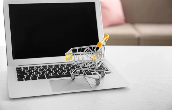 Ordenador portátil y pequeño carrito de compras en la mesa. Concepto de compras por Internet —  Fotos de Stock