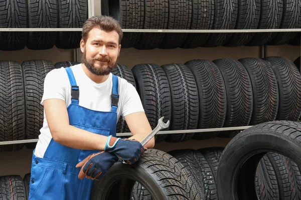 Mecánico masculino con llave y neumático de coche en la tienda de automóviles — Foto de Stock